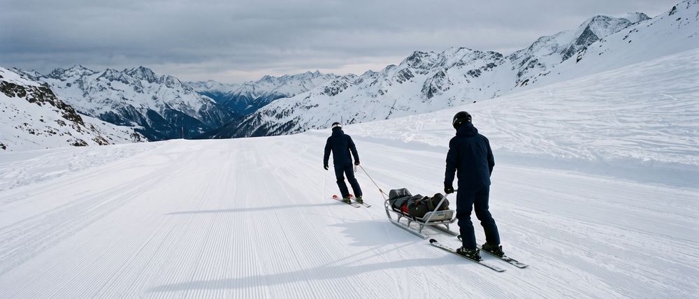 Deux pisteurs tirent une barquette de secours sur une piste damée.