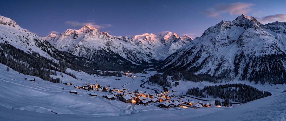 Une vallée sombre au crépuscule, les lumières d’un village allumées au fond.